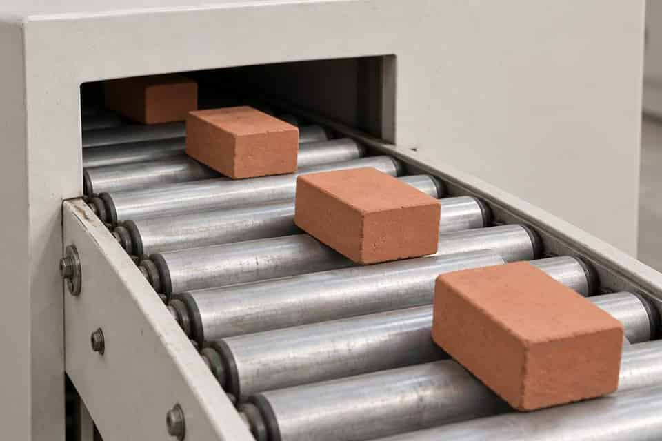Separate terracotta blocks move through an open aperture on a roller conveyor.